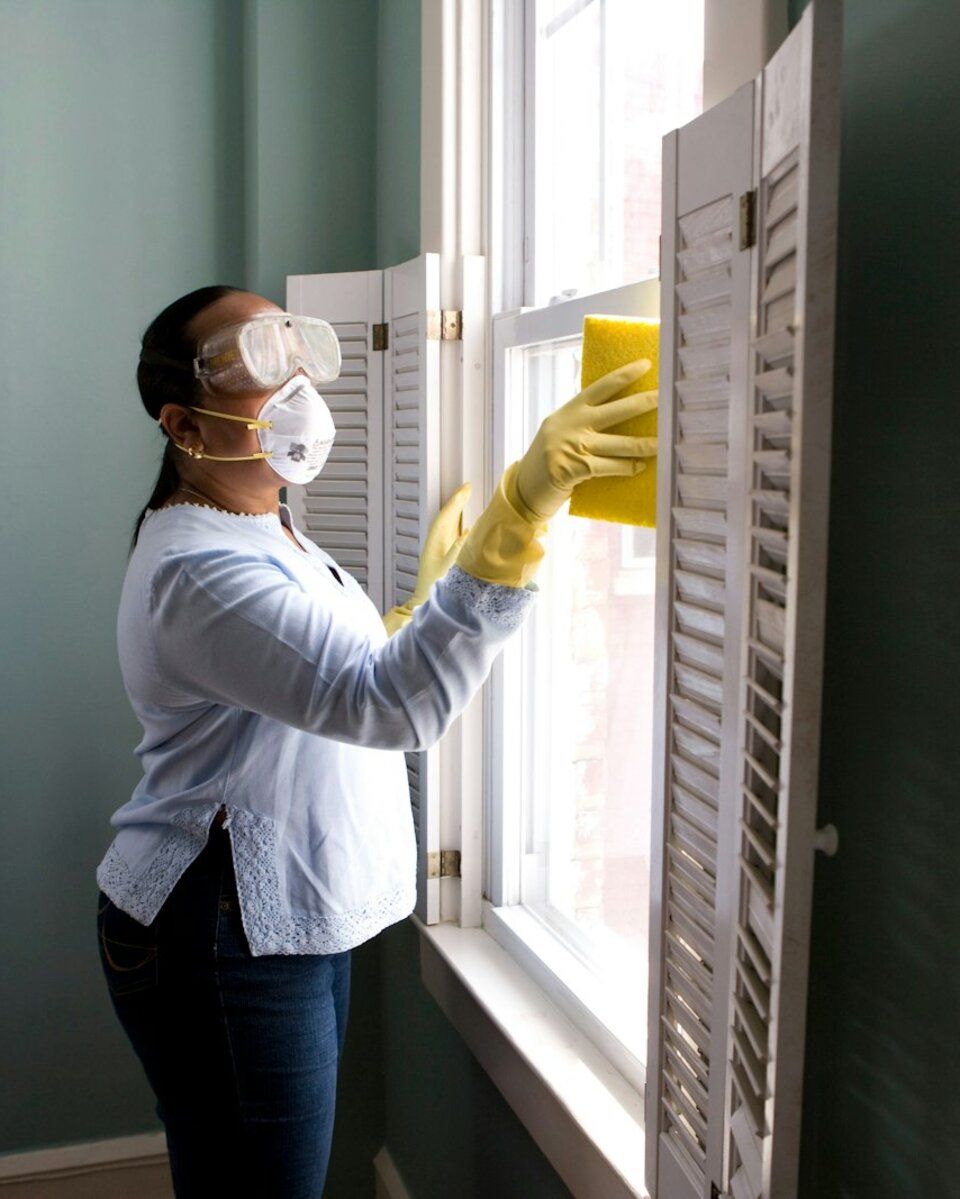 Profesional de la limpieza con guantes limpiando una ventana